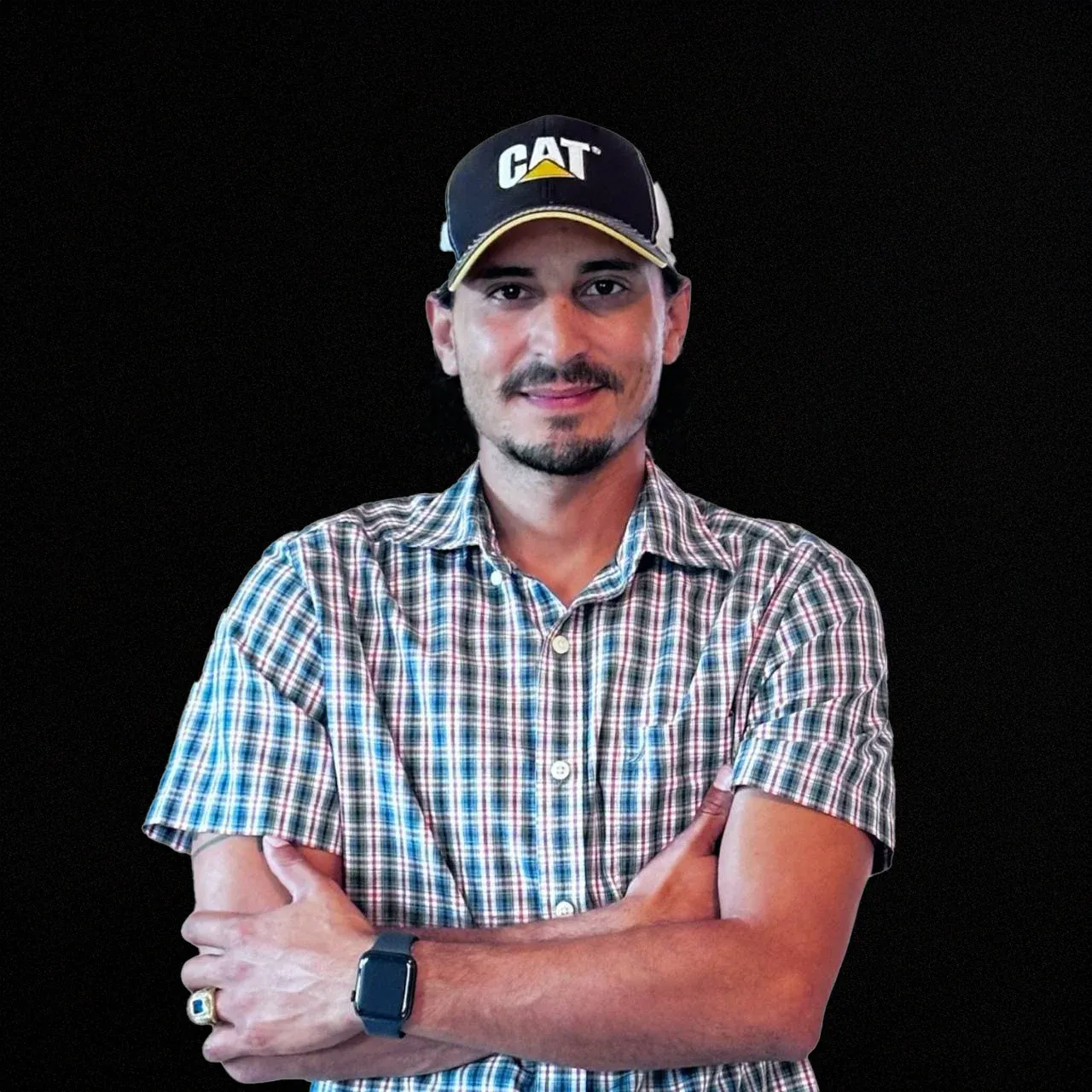 Hector Vargas, founder of Hector Tractor LLC, wearing a CAT cap with his arms crossed